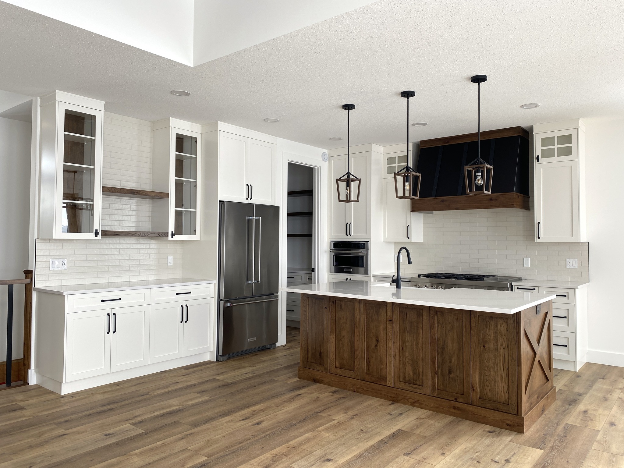Modern kitchen with white cabinets, stainless steel appliances, and a large wooden island. Pendant lights hang above, and the floor is light wood.