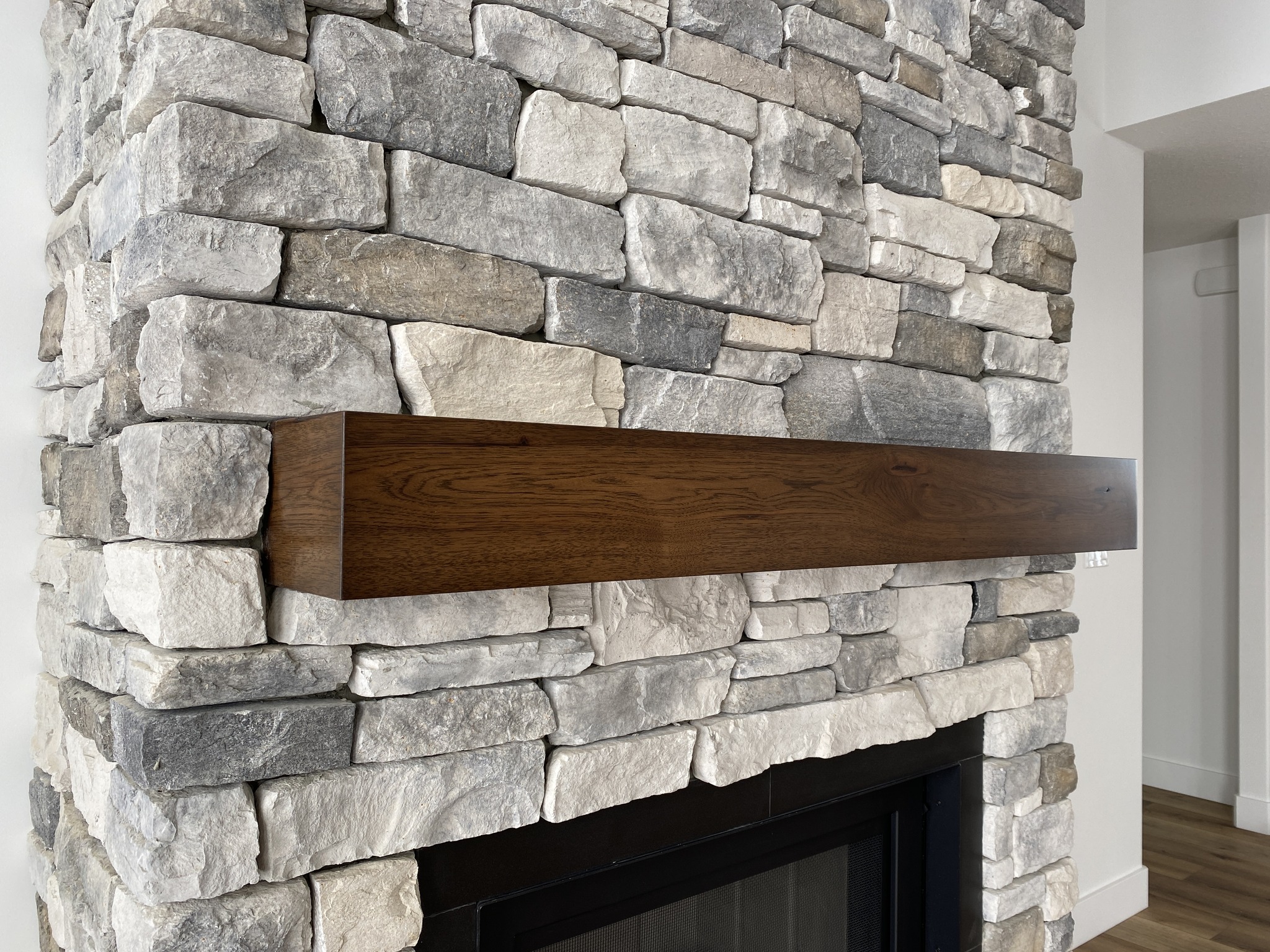 Stone fireplace with light gray and beige stones, featuring a sleek dark wooden mantel. The setting has a cozy, warm tone.