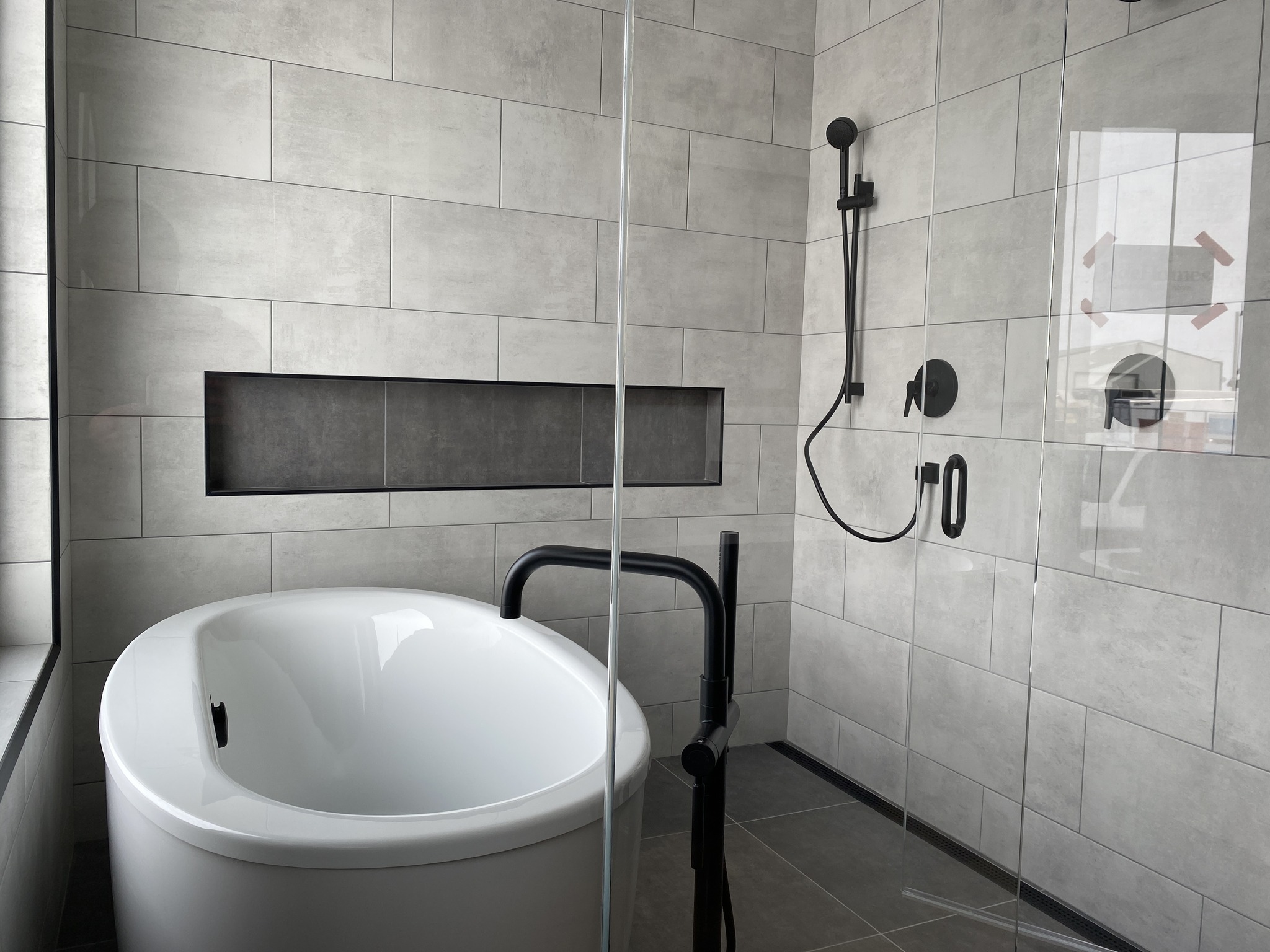 Modern bathroom with a white freestanding tub, black fixtures, and a glass-enclosed shower. Light gray tiles create a sleek, minimalist ambiance.