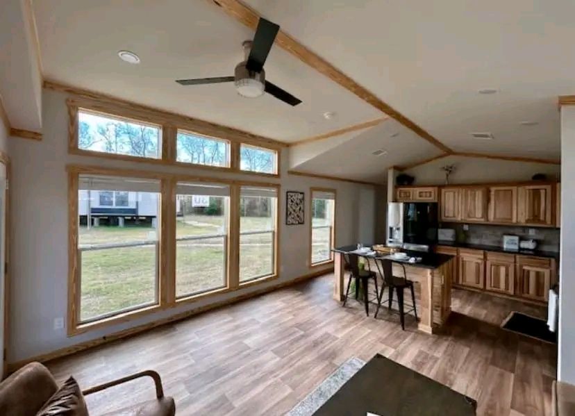Spacious living area with large windows, wood flooring, and a ceiling fan. View of a modern kitchen with wooden cabinets and a small island with stools.