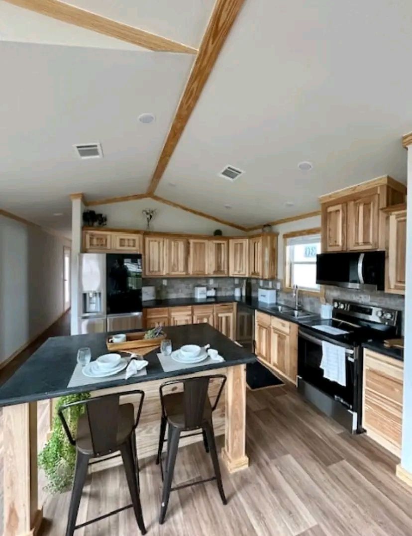 Spacious kitchen with a wooden ceiling and cabinets, black countertops, and a center island set with plates and glasses. Modern appliances enhance the cozy ambiance.