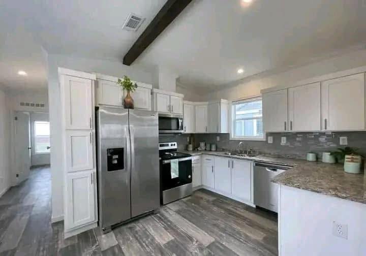Modern kitchen with white cabinets, stainless steel appliances, and wood-accented flooring. Bright lighting and a potted plant add a fresh touch.
