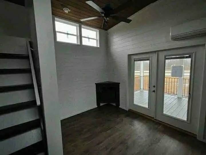 Cozy room with dark wooden floor, white walls, and a high ceiling. It features French doors leading to a balcony, and a small staircase on the side.