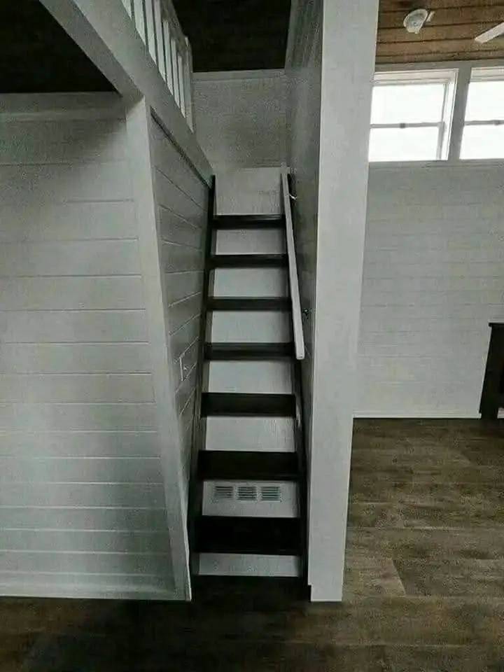 Narrow wood stairs with a white railing ascend to a loft in a modern interior. The minimal design is complemented by white walls and wood floors.