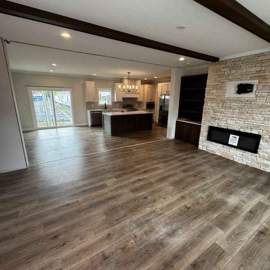 Spacious open concept living area with dark wood floors, stone accent wall, and modern kitchen featuring an island. Bright via glass doors. Cozy and inviting.