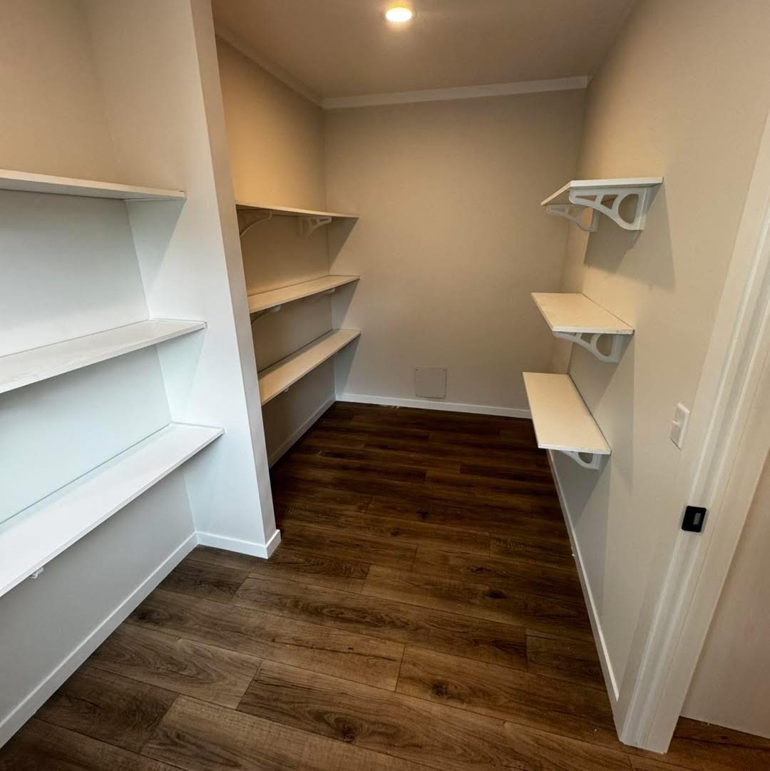 Walk-in pantry with wooden floors and white shelves on both sides. Soft lighting creates a clean, organized, and spacious feel.