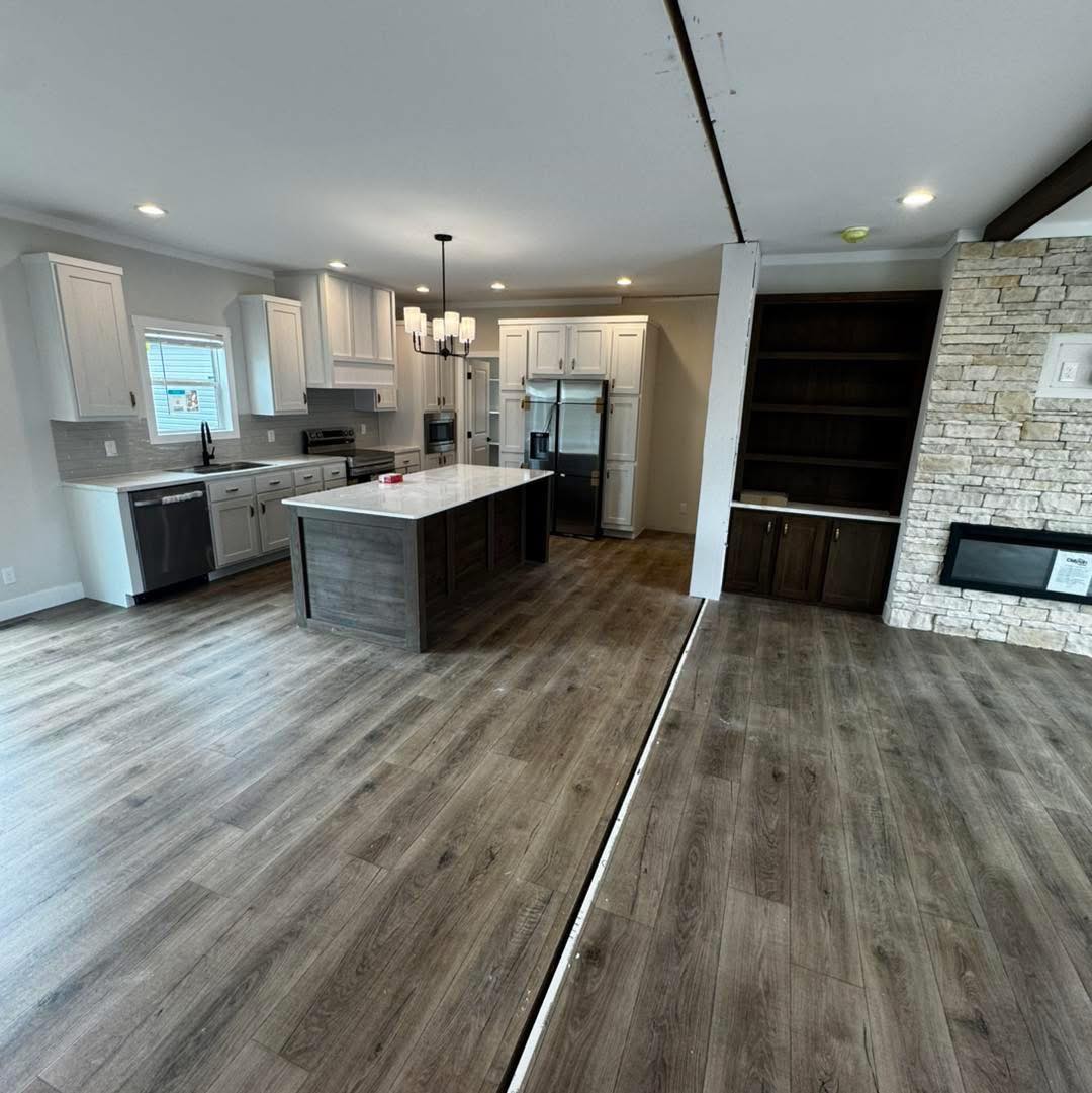 Modern kitchen with wood flooring, white cabinets, a dark wood island with white marble top, stainless steel appliances, and a stone accent wall.
