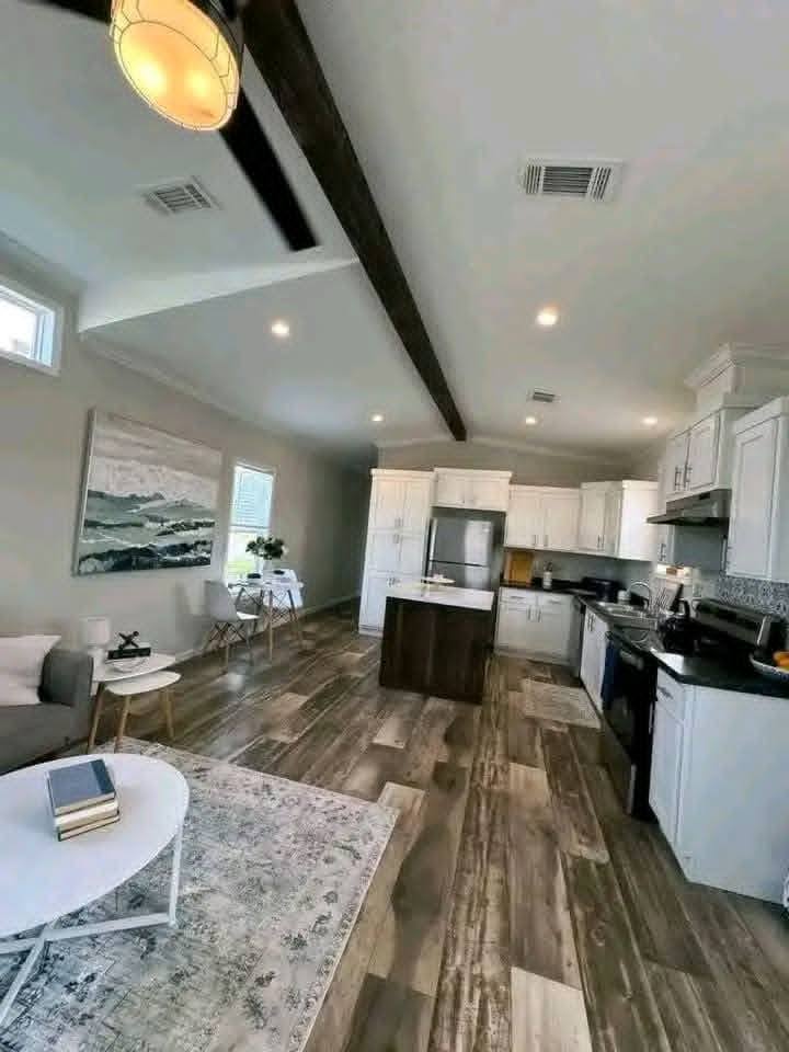 Modern open-concept kitchen and living area with wooden floors, white cabinets, and a gray sofa. Bright, airy atmosphere with large wall art.