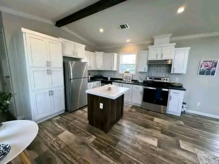 Modern kitchen with white cabinets, stainless steel appliances, and a small island. Wooden flooring and soft lighting create a cozy atmosphere.