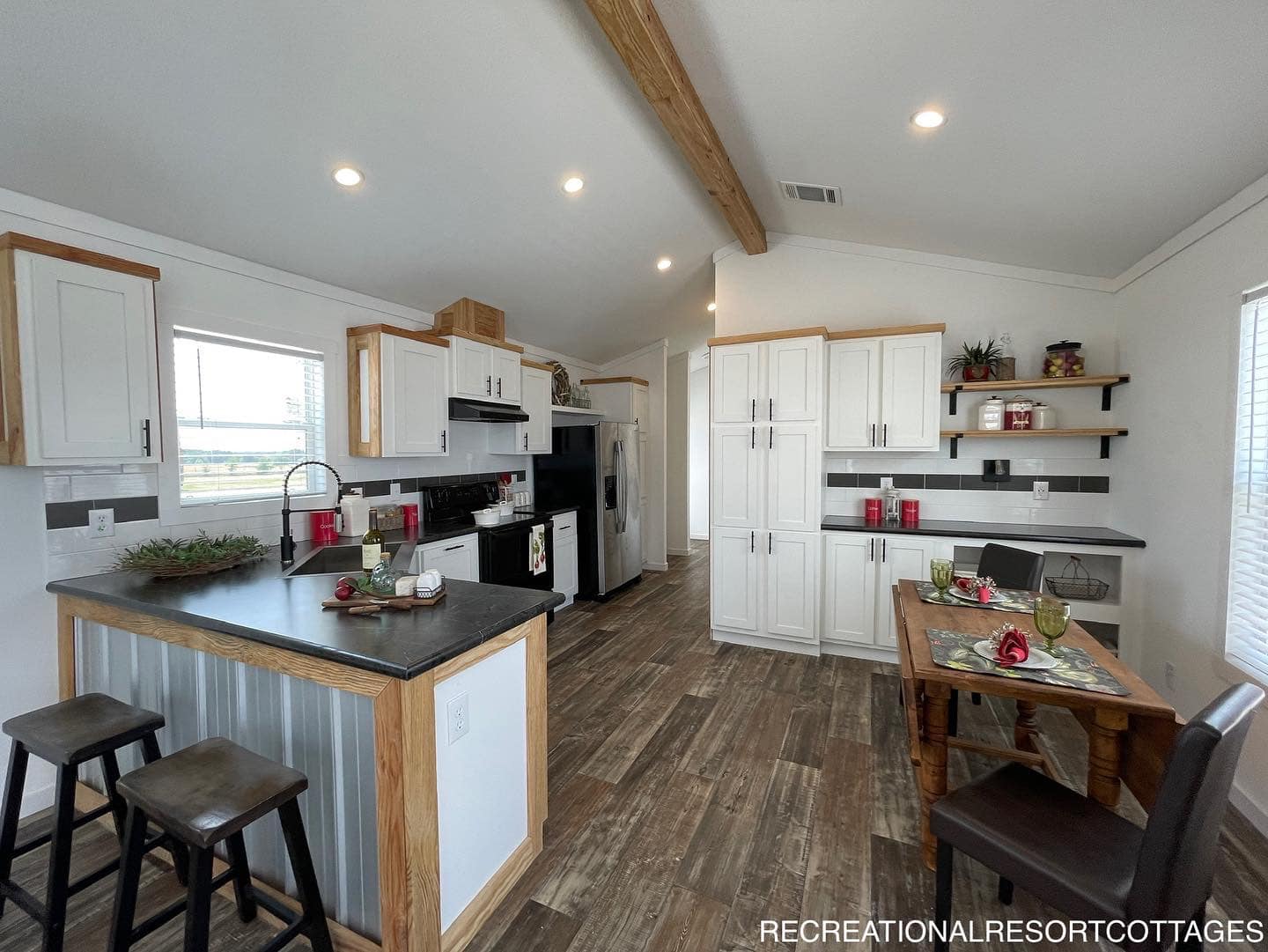 Modern kitchen with dark countertops, white cabinets, and wood accents. A small dining table with red and green décor creates a cozy, inviting atmosphere.