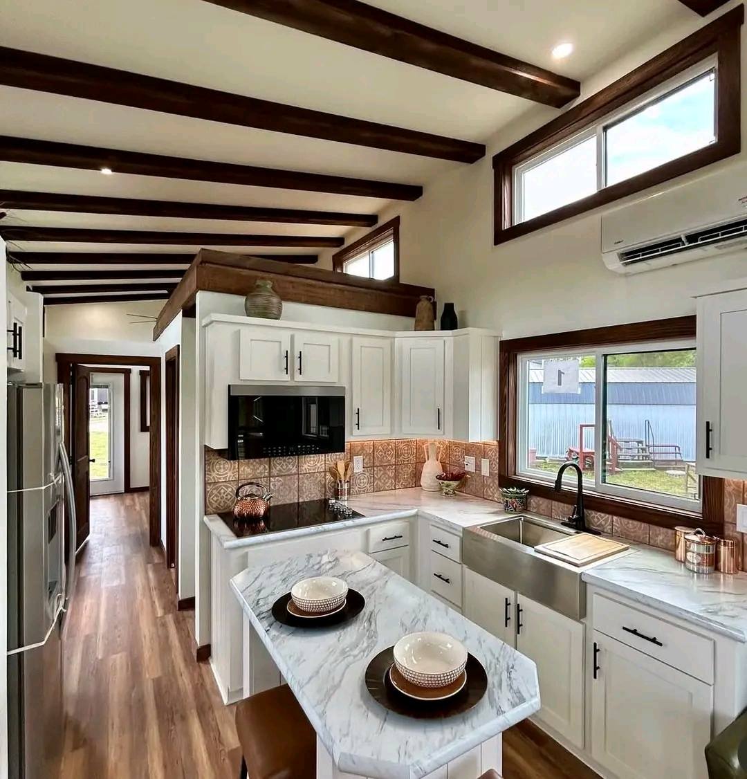 Stylish kitchen with white cabinets, marble countertops, and exposed wood beams. A cozy breakfast nook with two place settings on an island. Airy and bright.