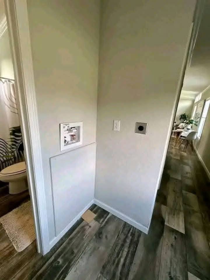 Unfinished wall outlet and central vacuum inlet on a hallway wall; bathroom visible on the left. Floor features wood-like tile, creating a modern feel.