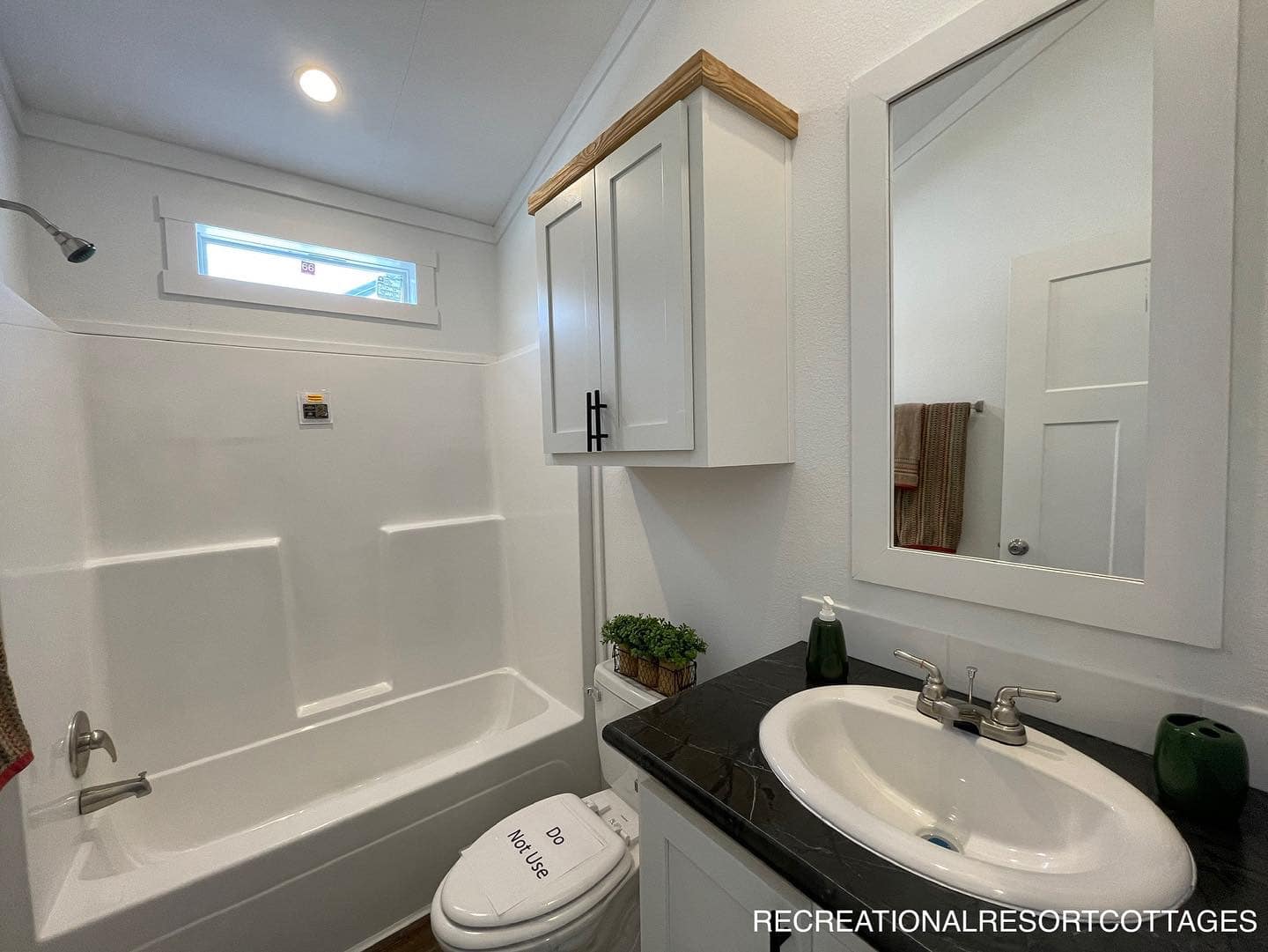 Bright, modern bathroom with a white bathtub, overhead shower, and small window. Features a black countertop, white sink, and sleek cabinetry.