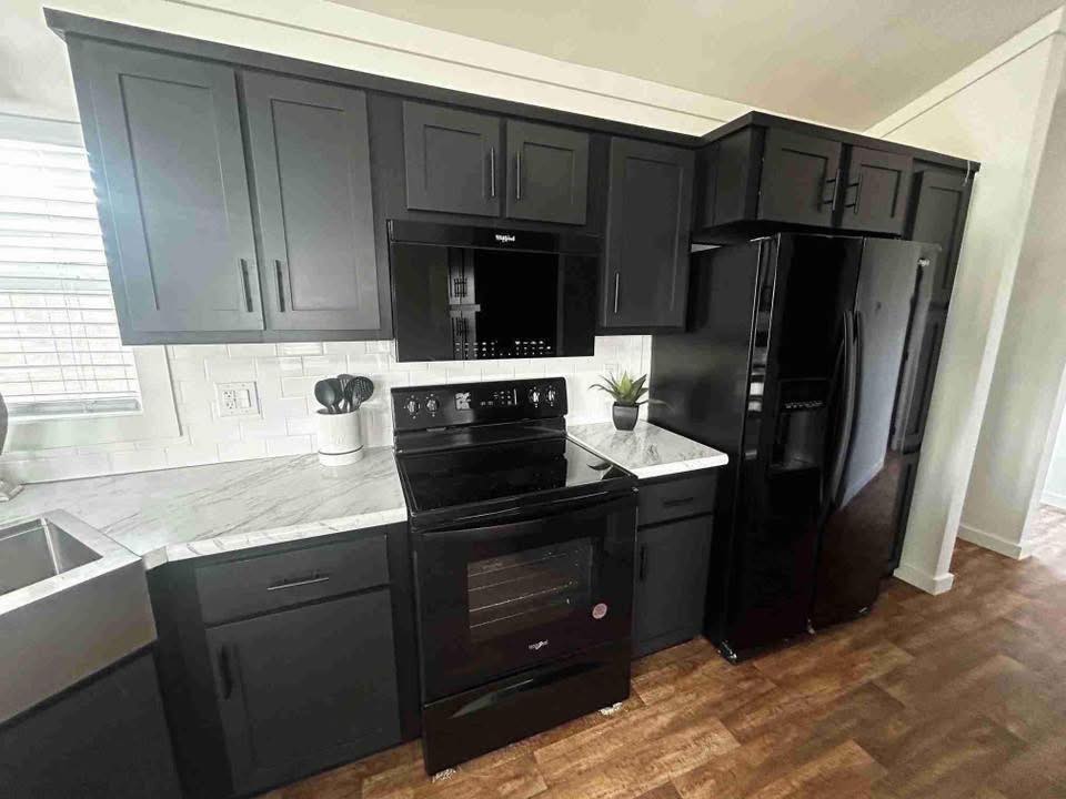 Modern kitchen with sleek black cabinets, matching appliances, and white marble countertops. A small plant and utensil holder add a touch of decor.