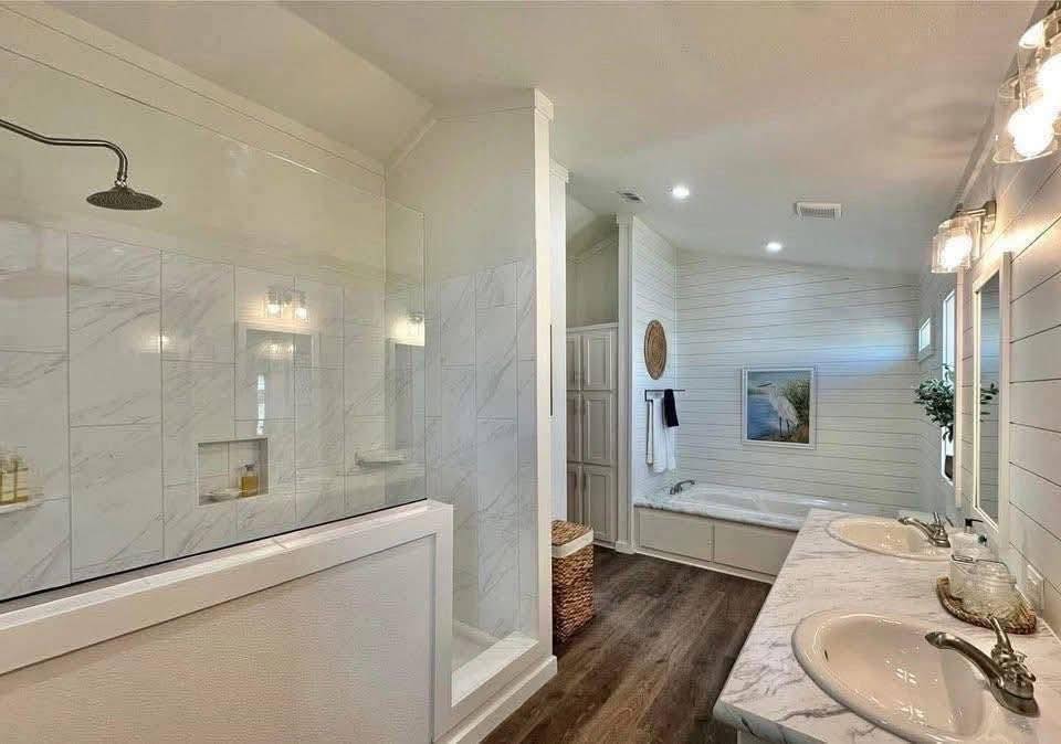 Spacious bathroom with a marble-counter double sink, large walk-in shower, and a bathtub. The design is modern and elegant with warm lighting.