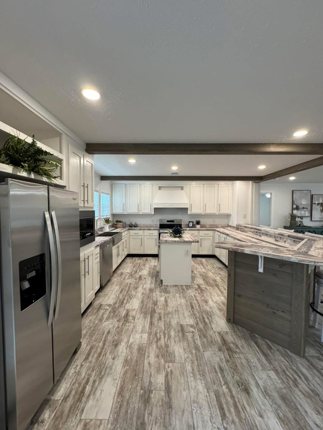Spacious modern kitchen with white cabinets, stainless steel appliances, and a large island with granite countertop. Cozy lighting and wooden floor add warmth.