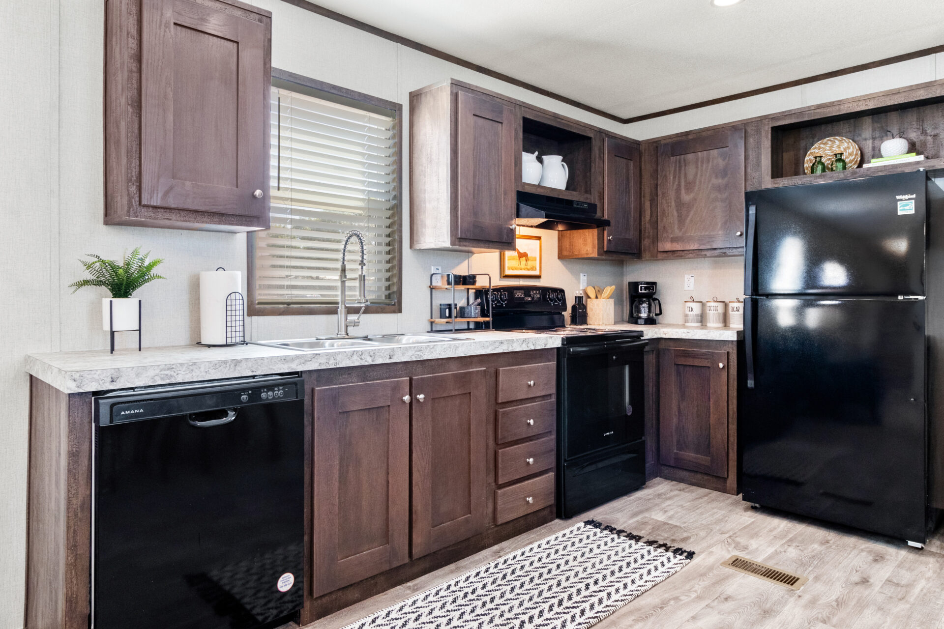 Modern kitchen with dark wood cabinets, marble countertops, and black appliances, including a dishwasher and fridge. A patterned rug adds warmth.