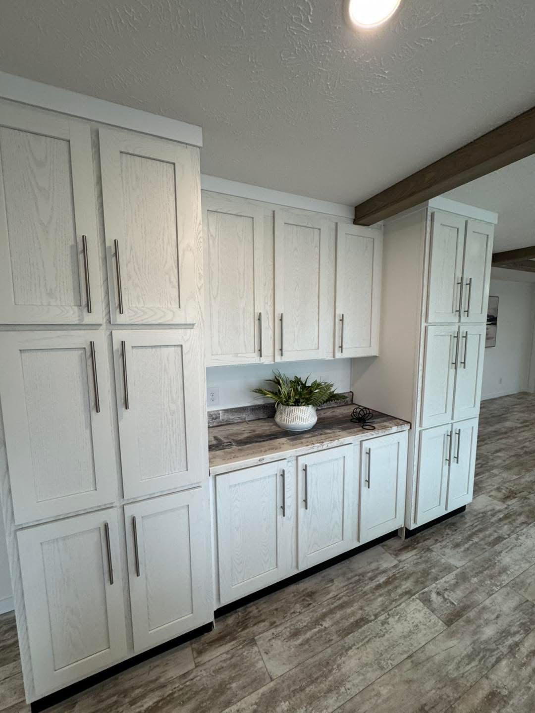Bright kitchen space featuring white cabinets with sleek silver handles, wood-textured flooring, and a countertop with a potted plant adding a touch of freshness.