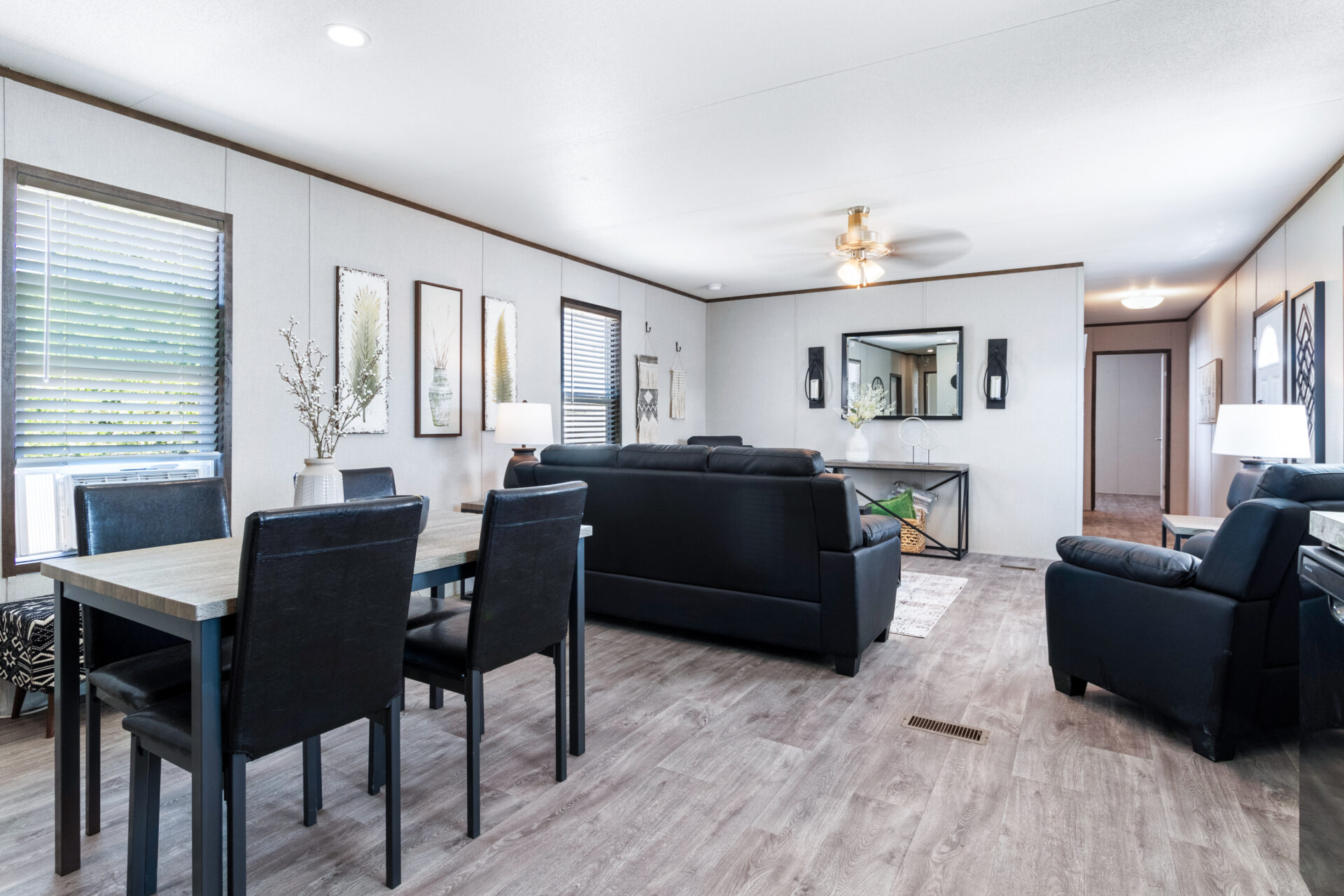 A modern, open-plan living and dining area with light wood floors, black furniture, and minimalist decor. Soft lighting creates a cozy atmosphere.