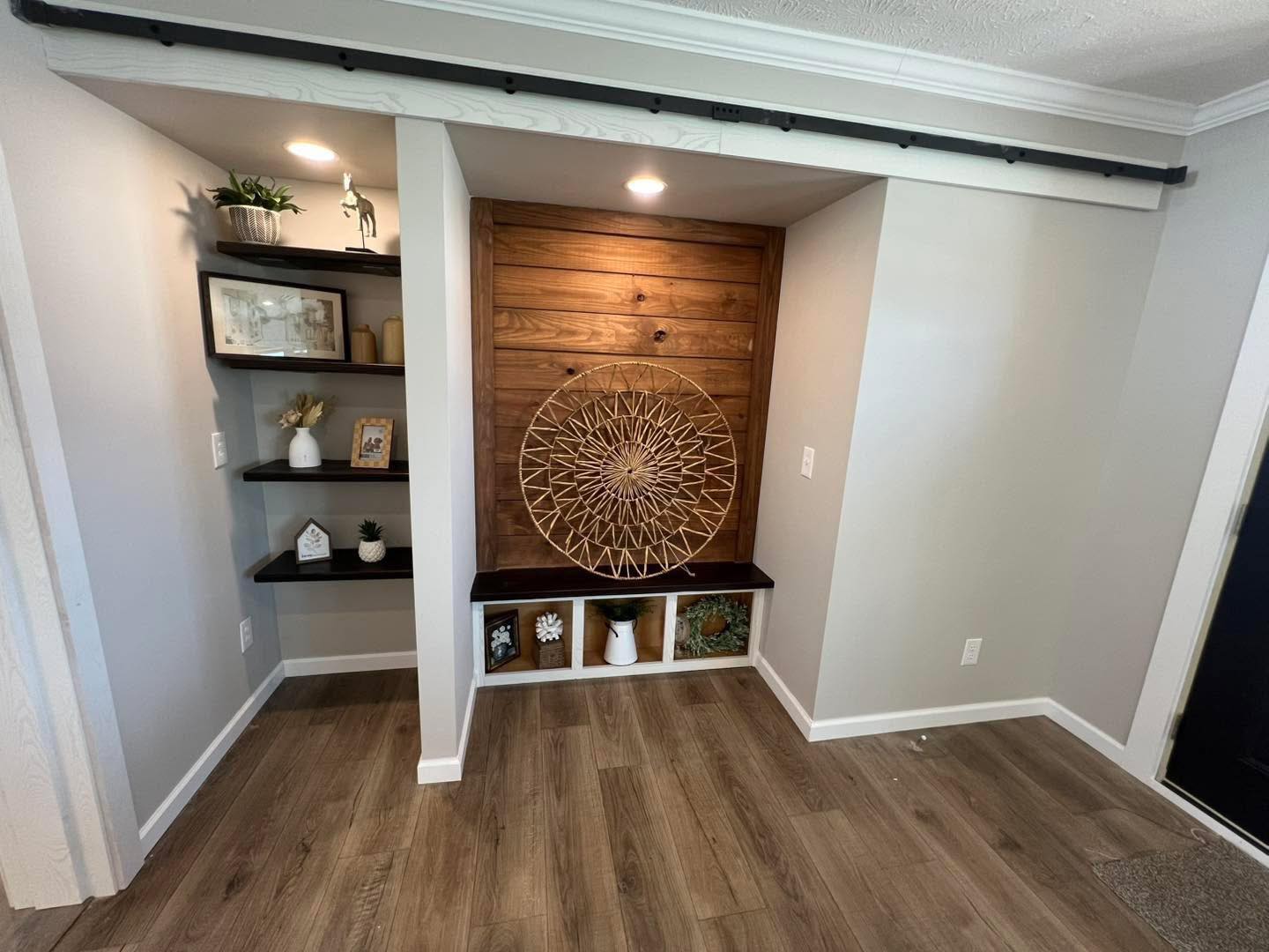 Small alcove with wood paneling and decorative shelves. Features a woven circular wall art, plants, and vases, creating a cozy, modern feel.