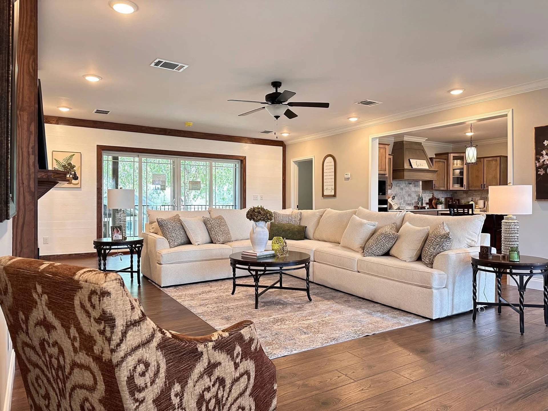 Spacious living room with a large beige sectional sofa, decorative cushions, and a round coffee table. Warm lighting and wood flooring create a cozy ambiance.