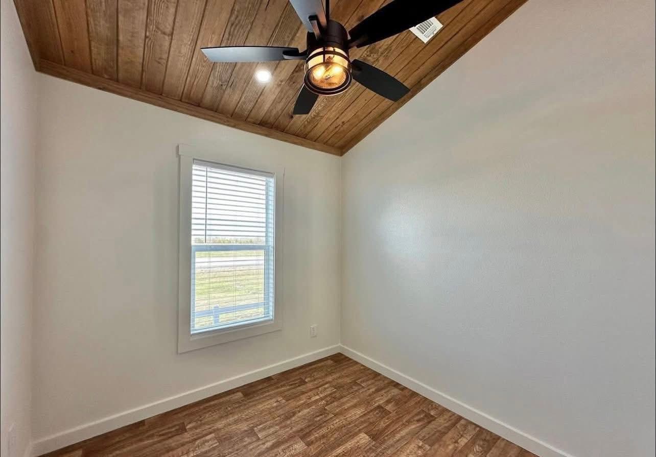 Small minimalist room with a wood-paneled ceiling, modern black ceiling fan, and window with blinds. Natural light creates a warm, inviting ambiance.