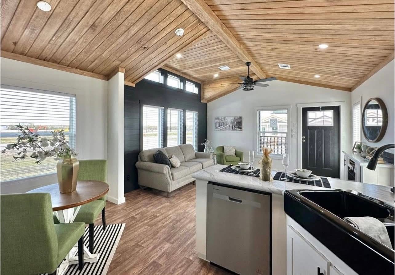Stylish open-concept living area with wood-paneled ceiling, modern kitchen, cozy seating, and large windows. Light, airy, and inviting atmosphere.