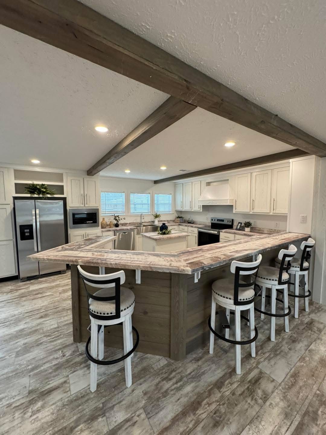 Spacious modern kitchen with a large, U-shaped marble island, four high-backed white bar stools, stainless steel appliances, and white cabinets, exuding a warm, inviting ambiance.