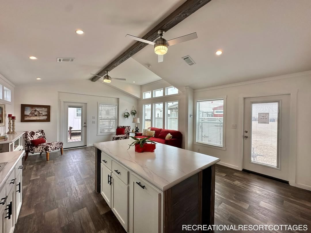 Modern, bright living room with high ceilings, white walls, and wood accents. Features a red sofa, island kitchen, and ample natural light. Cozy and inviting.