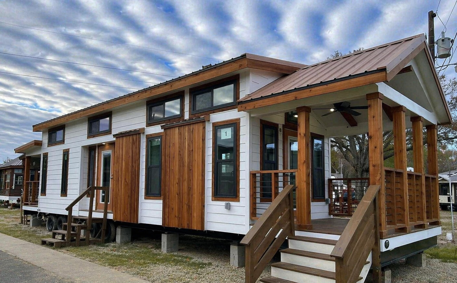 Modern tiny house with white and wood siding, featuring large windows and a small covered porch. A cloudy sky creates a serene backdrop.