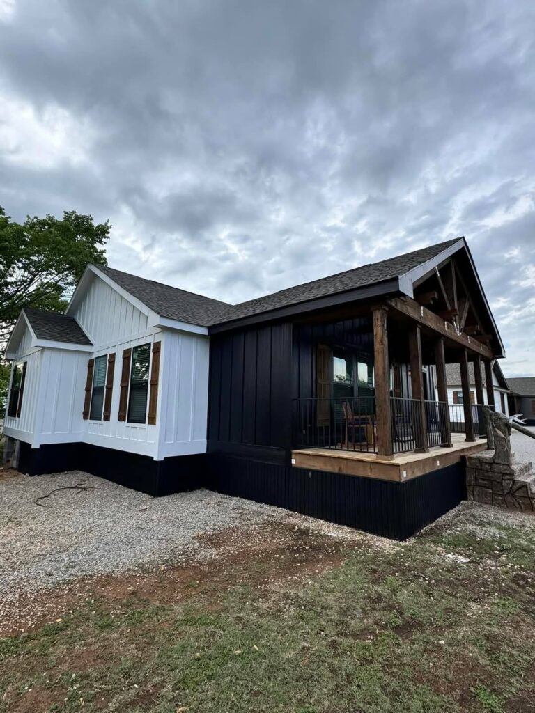 Modern farmhouse with contrasting white and dark exterior is set against a cloudy sky. Wooden porch beams add rustic charm to the serene scene.