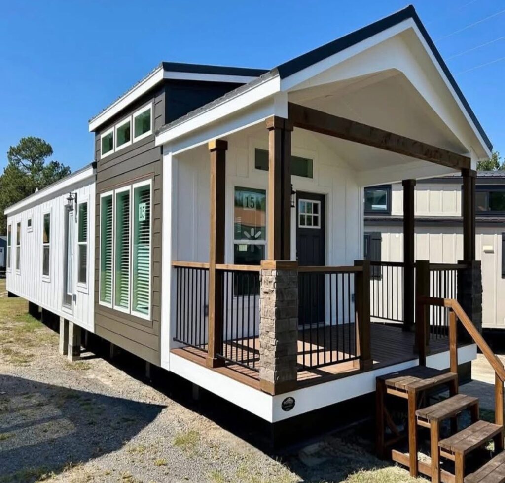 Modern tiny home with a white and brown exterior, featuring large windows and a cozy porch with wooden railings, set against a clear blue sky.