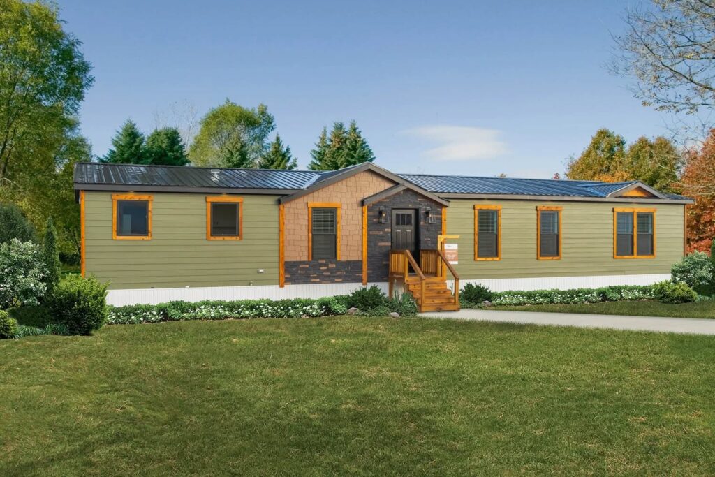 A modern green manufactured home with a black roof, wood accents, and front porch. It's surrounded by lush trees and a manicured lawn.