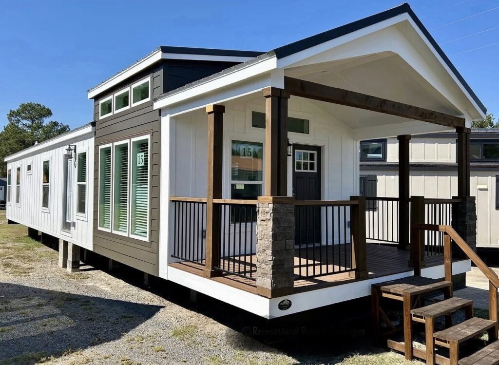 Stylish tiny house with a modern exterior features large windows, a covered porch, and wooden accents. It's set on gravel, evoking a cozy, inviting vibe.
